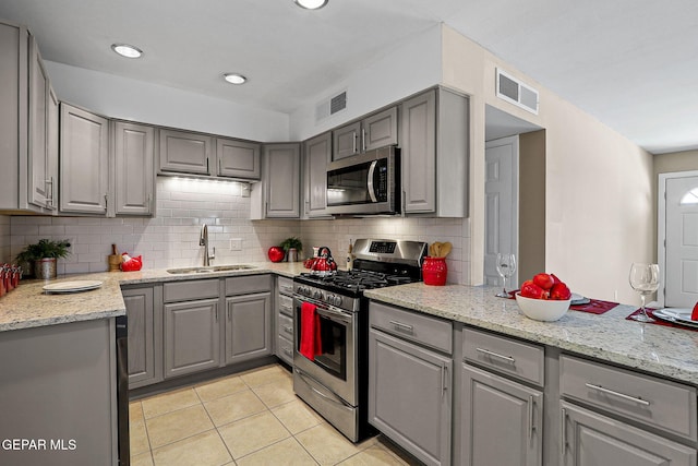 kitchen featuring light stone countertops, appliances with stainless steel finishes, gray cabinets, and sink