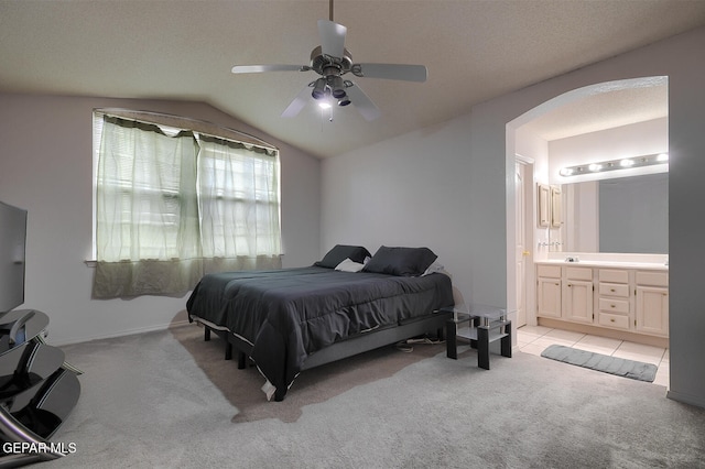 carpeted bedroom with ceiling fan, ensuite bathroom, and vaulted ceiling