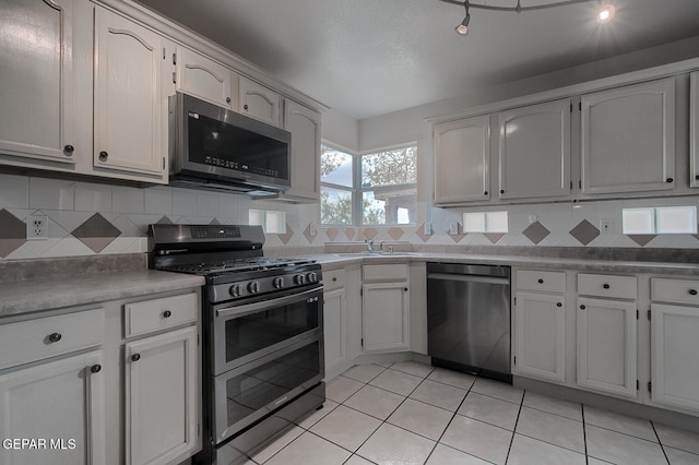 kitchen with light tile patterned floors, sink, white cabinetry, backsplash, and stainless steel appliances