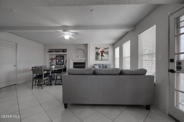 tiled living room with ceiling fan, built in features, and a textured ceiling