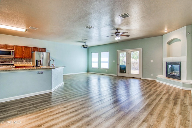 unfurnished living room with ceiling fan, a fireplace, light wood-type flooring, and a textured ceiling