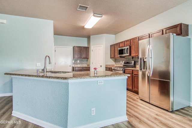 kitchen with tasteful backsplash, sink, appliances with stainless steel finishes, and light hardwood / wood-style flooring