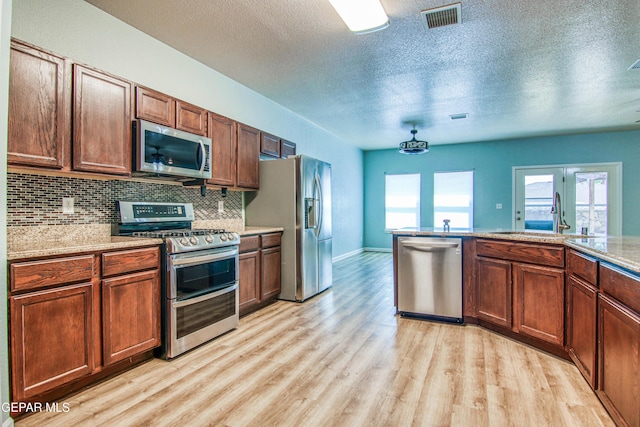 kitchen featuring sink, stainless steel appliances, tasteful backsplash, a textured ceiling, and light wood-type flooring