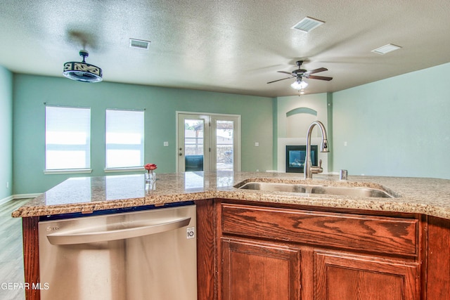 kitchen featuring sink, light hardwood / wood-style flooring, stainless steel dishwasher, ceiling fan, and a textured ceiling