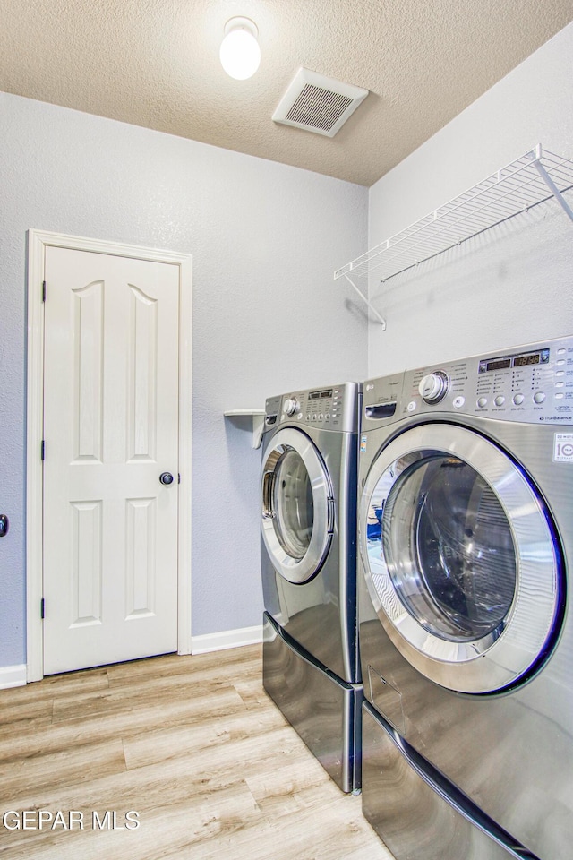 laundry area featuring washing machine and dryer, light wood-type flooring, and a textured ceiling