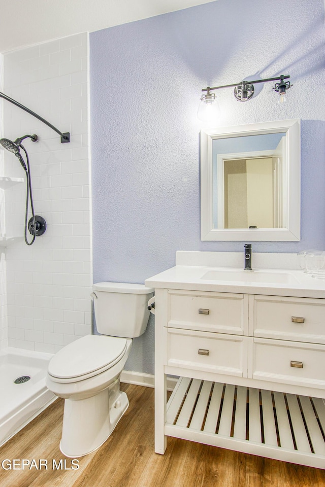 bathroom featuring hardwood / wood-style floors, vanity, toilet, and tiled shower