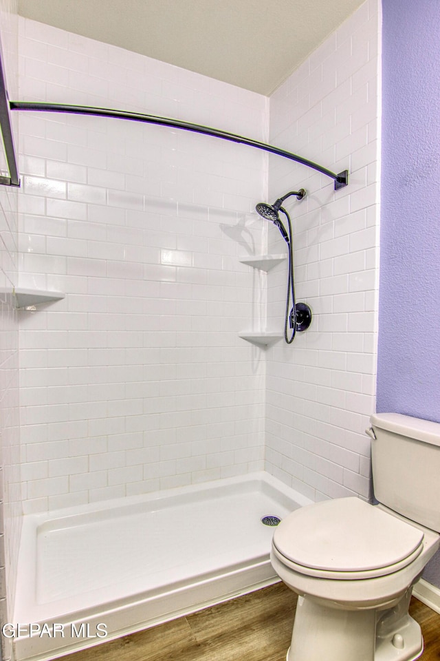 bathroom with toilet, hardwood / wood-style floors, and tiled shower