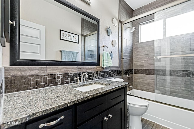 full bathroom featuring combined bath / shower with glass door, backsplash, vanity, hardwood / wood-style flooring, and toilet