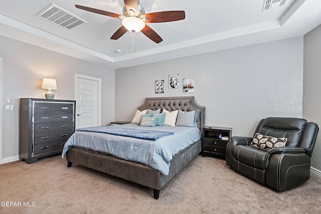 bedroom with a raised ceiling, light carpet, and ceiling fan