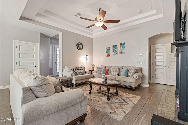 living room with hardwood / wood-style flooring, ceiling fan, and a raised ceiling