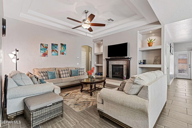 living room with a raised ceiling, built in features, and hardwood / wood-style flooring