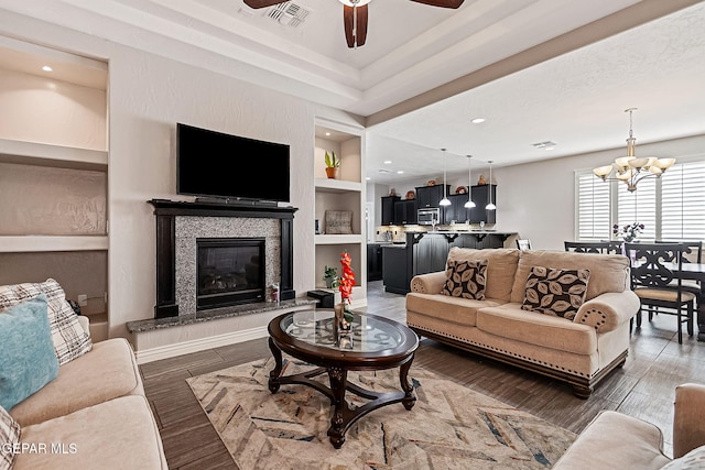 living room featuring built in shelves, ceiling fan with notable chandelier, and dark wood-type flooring