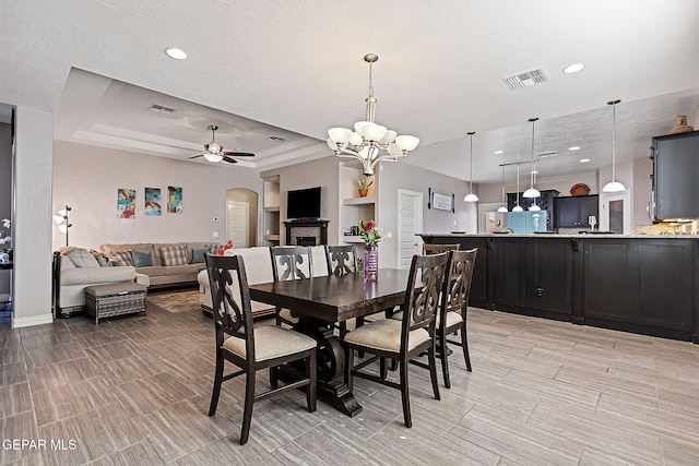 dining area with ceiling fan with notable chandelier and a tray ceiling