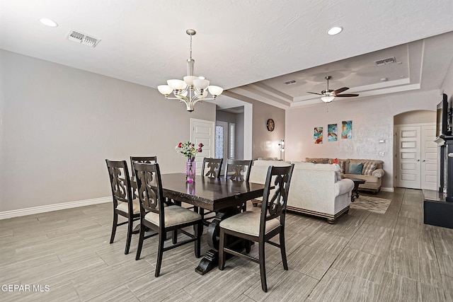 dining area with ceiling fan with notable chandelier, a raised ceiling, and light hardwood / wood-style flooring