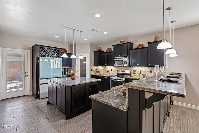 kitchen with hanging light fixtures, a kitchen breakfast bar, dark stone counters, a kitchen island, and appliances with stainless steel finishes