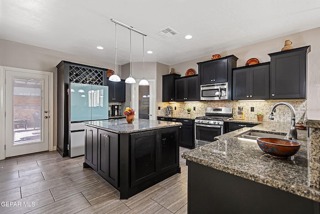 kitchen with appliances with stainless steel finishes, sink, pendant lighting, dark stone countertops, and a kitchen island