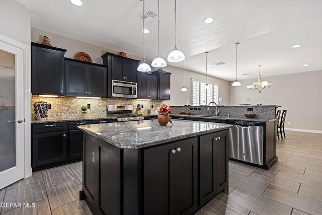 kitchen with sink, hanging light fixtures, appliances with stainless steel finishes, a kitchen island, and a chandelier