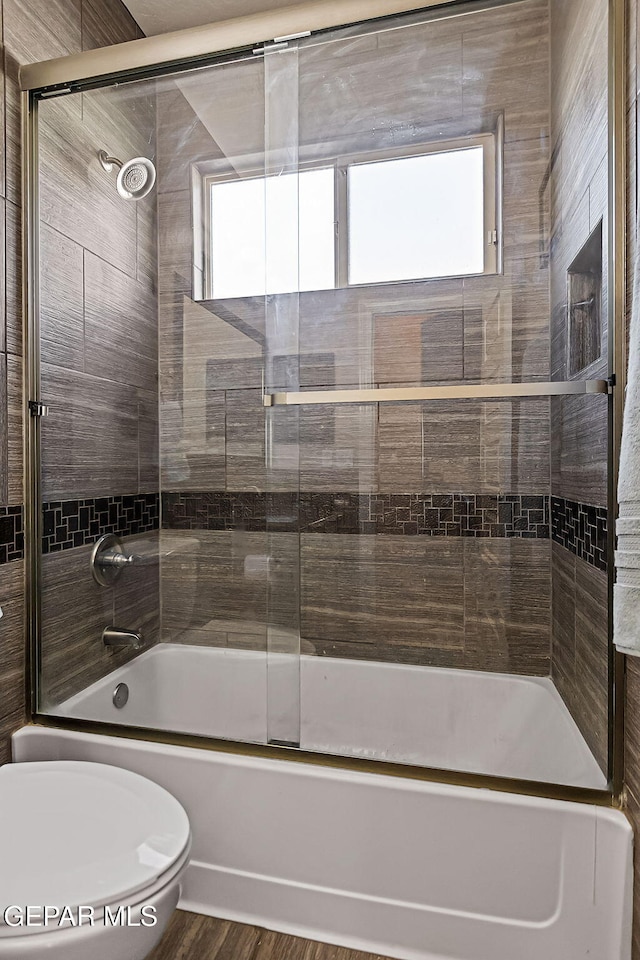 bathroom featuring toilet, wood-type flooring, and combined bath / shower with glass door