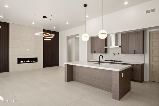 kitchen featuring sink, an island with sink, decorative light fixtures, and wall chimney range hood