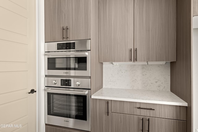 kitchen featuring light brown cabinets, light stone counters, backsplash, and double oven