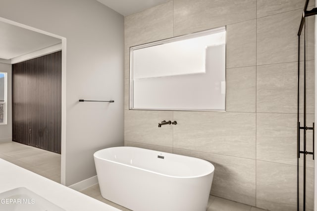 bathroom with tile patterned floors, a bath, and tile walls