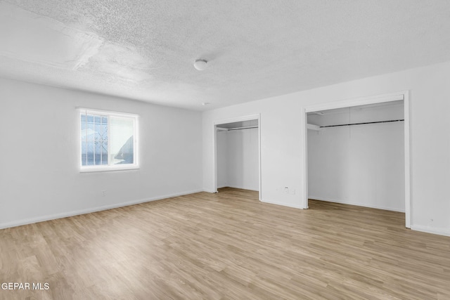 unfurnished bedroom with multiple closets, a textured ceiling, and light hardwood / wood-style flooring