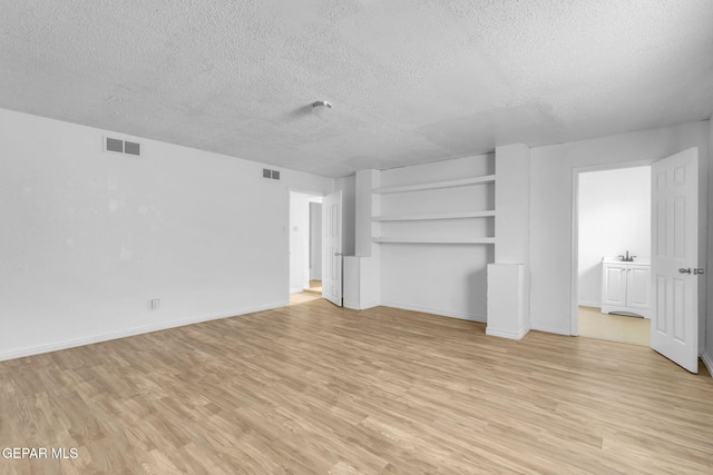 unfurnished living room with sink, a textured ceiling, and light hardwood / wood-style flooring