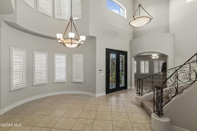 entrance foyer featuring ceiling fan with notable chandelier, light tile patterned flooring, and a high ceiling