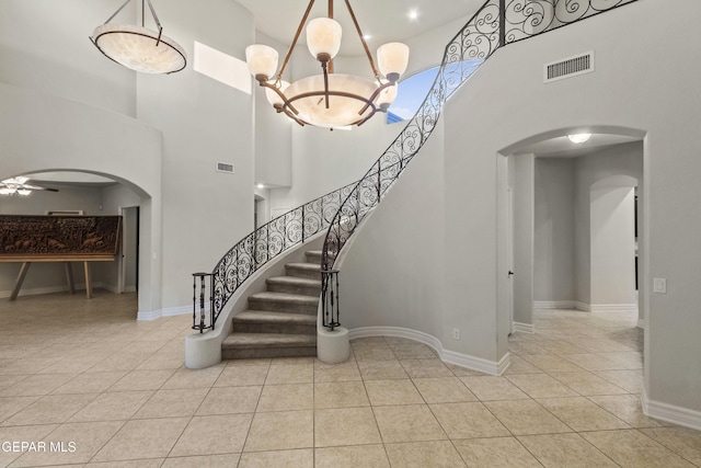 staircase with tile patterned flooring, ceiling fan with notable chandelier, and a high ceiling