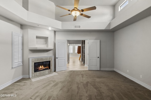 unfurnished living room featuring a tray ceiling, carpet floors, a high ceiling, and a tiled fireplace