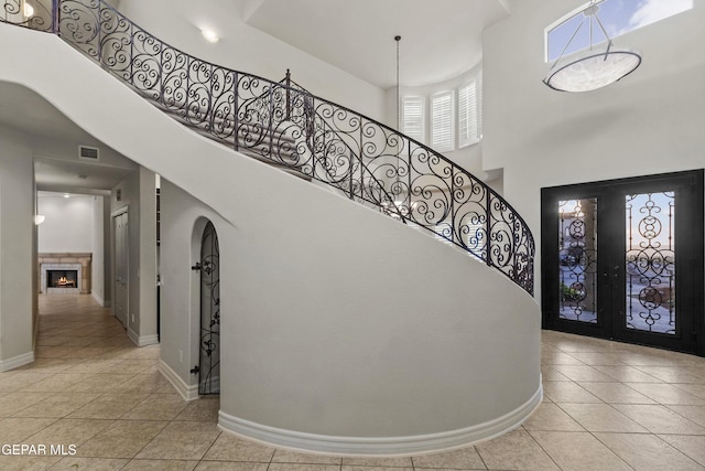 foyer with french doors, a fireplace, light tile patterned floors, and a high ceiling