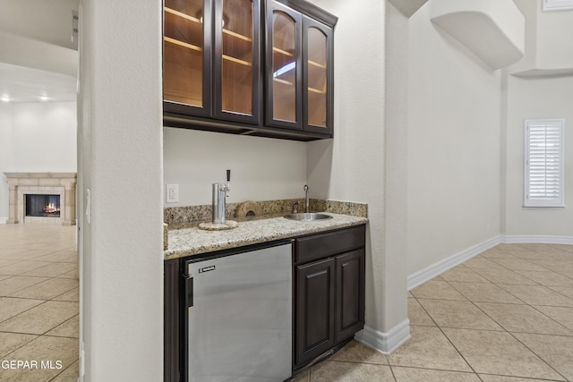 bar featuring dark brown cabinets, sink, stainless steel refrigerator, and light tile patterned flooring