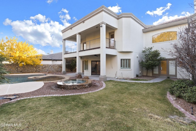 back of house featuring a lawn, a swimming pool with hot tub, a balcony, and french doors