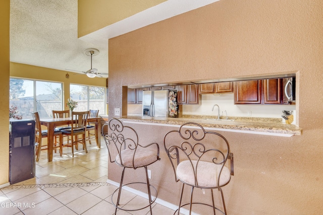 kitchen with ceiling fan, stainless steel appliances, kitchen peninsula, a textured ceiling, and light tile patterned floors