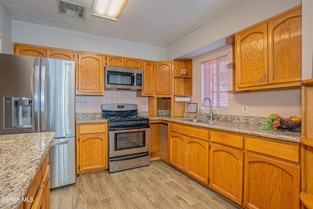 kitchen featuring sink, decorative backsplash, light wood-type flooring, light stone countertops, and appliances with stainless steel finishes