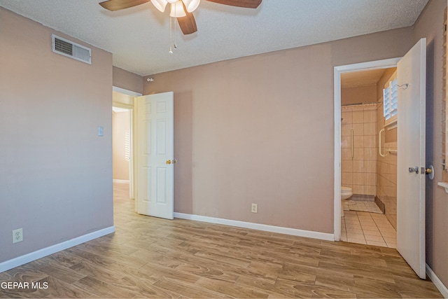 unfurnished bedroom with a textured ceiling, ensuite bath, light hardwood / wood-style flooring, and ceiling fan