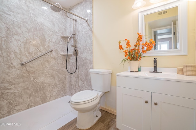 bathroom with a tile shower, hardwood / wood-style floors, vanity, and toilet