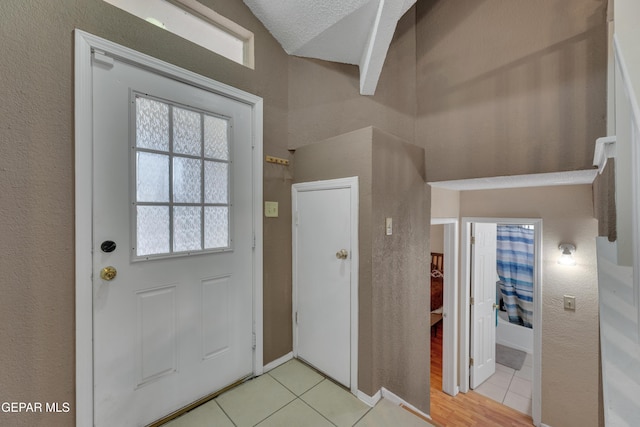 foyer featuring light tile patterned flooring, a textured ceiling, and vaulted ceiling