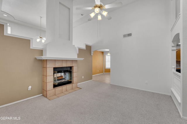 unfurnished living room featuring ceiling fan, light colored carpet, a high ceiling, and a tile fireplace