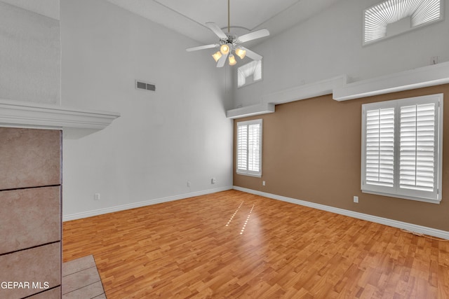 unfurnished living room with ceiling fan, a high ceiling, a healthy amount of sunlight, and light wood-type flooring