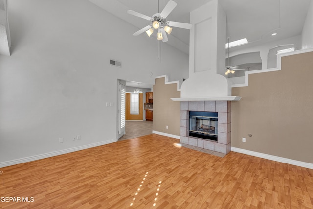 unfurnished living room with ceiling fan with notable chandelier, a tile fireplace, a towering ceiling, and light wood-type flooring