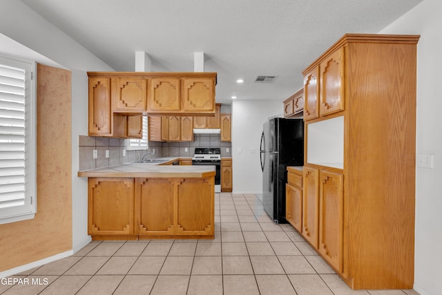 kitchen with black refrigerator, decorative backsplash, kitchen peninsula, light tile patterned floors, and stove