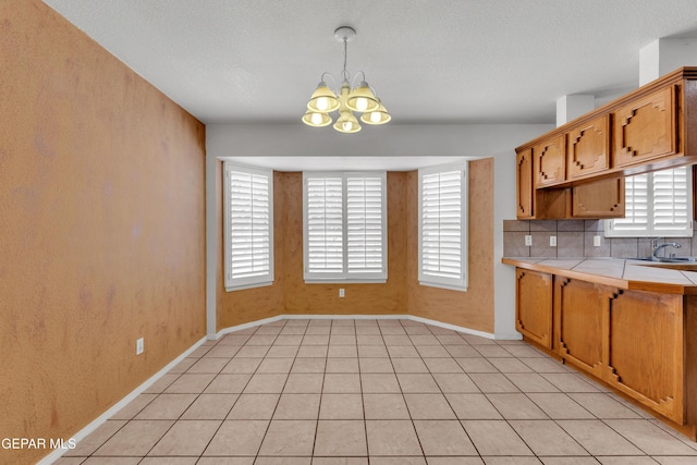 kitchen featuring an inviting chandelier, plenty of natural light, backsplash, tile countertops, and light tile patterned floors