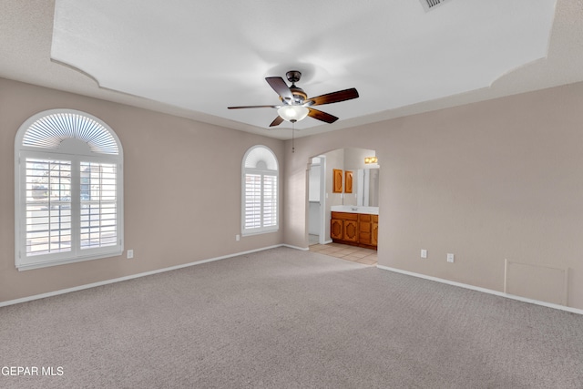 interior space with light carpet, ceiling fan, and ensuite bath