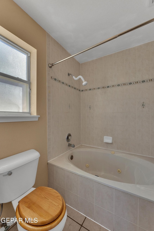 bathroom with toilet, tiled shower / bath combo, and tile patterned flooring