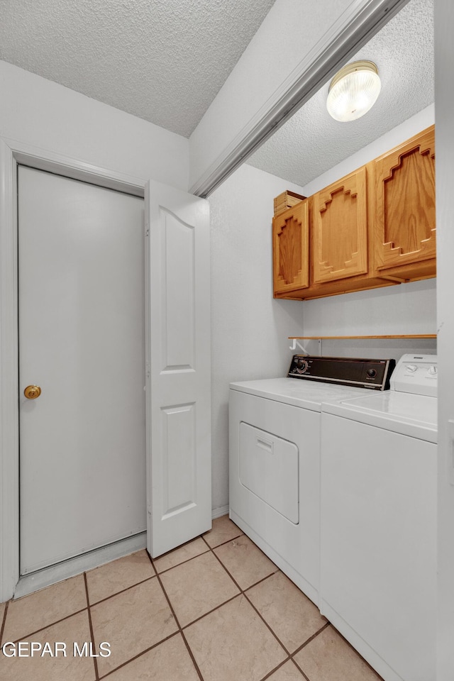 laundry area featuring light tile patterned floors, washer and dryer, a textured ceiling, and cabinets