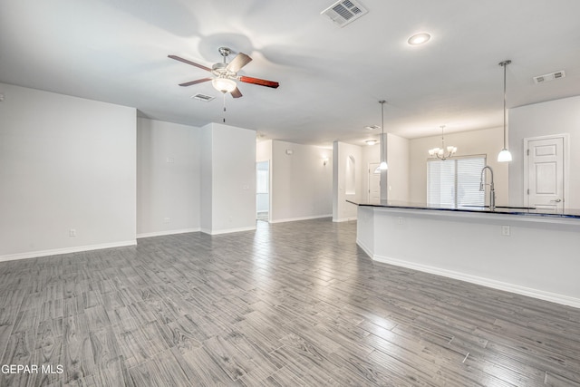 unfurnished living room with wood-type flooring, ceiling fan with notable chandelier, and sink