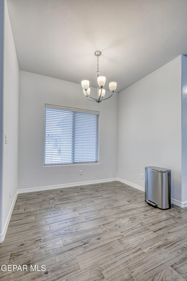 empty room with light hardwood / wood-style floors and a notable chandelier