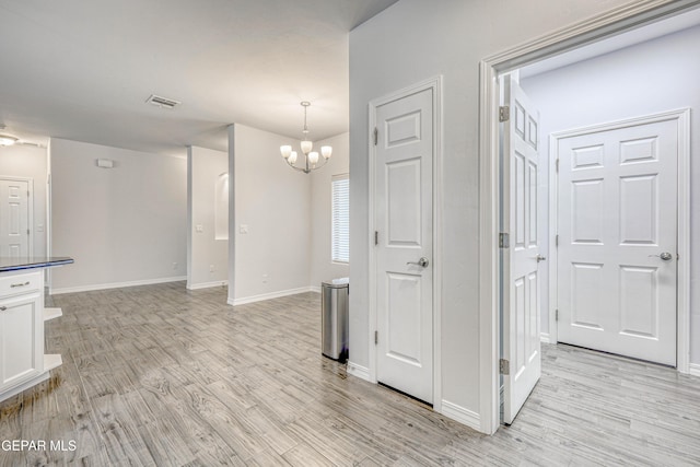 interior space featuring white cabinets, decorative light fixtures, an inviting chandelier, and light hardwood / wood-style flooring