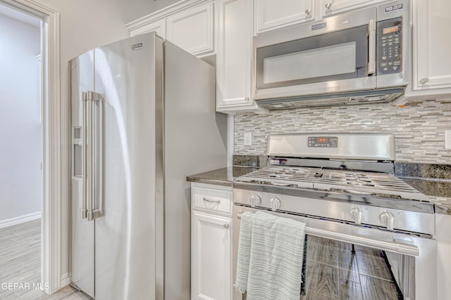 kitchen with white cabinets, stainless steel appliances, dark stone counters, and tasteful backsplash